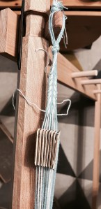 A picture showing warp threads running across the top of the warp weighted loom with several weaving 'cards' that create the shed. The band is about 1cm wide and the design is a series of  arrows running in the same direction. 